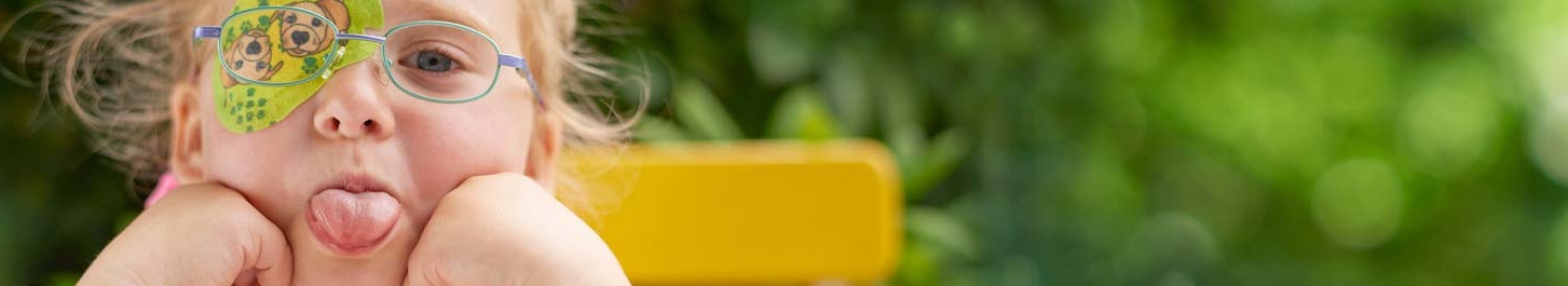 Kopafbeelding meisje met ORTOPAD®-oogpleister ‘honden’ steekt de tong uit